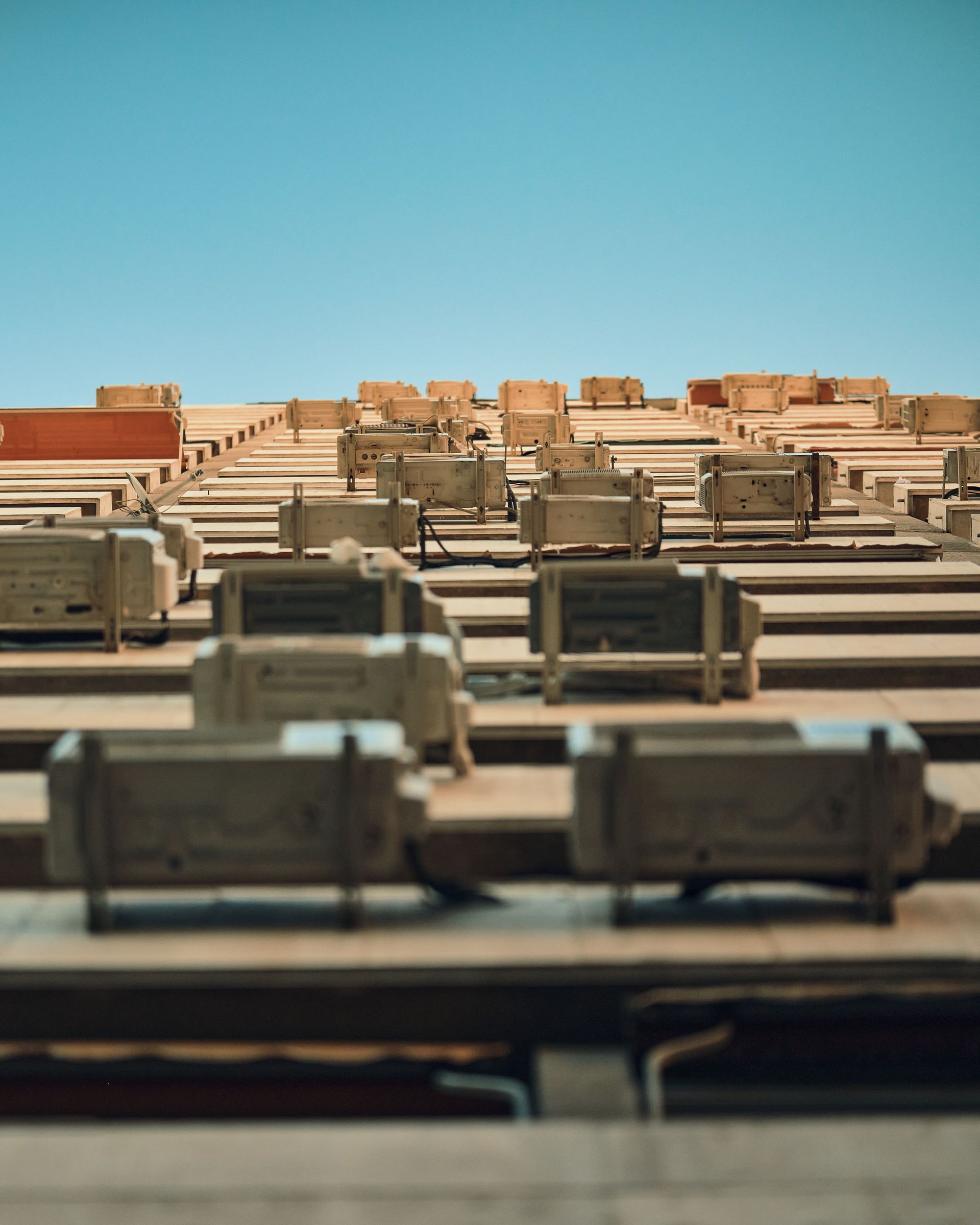 Low angle view of a building façade with multiple air conditioners against a clear sky.