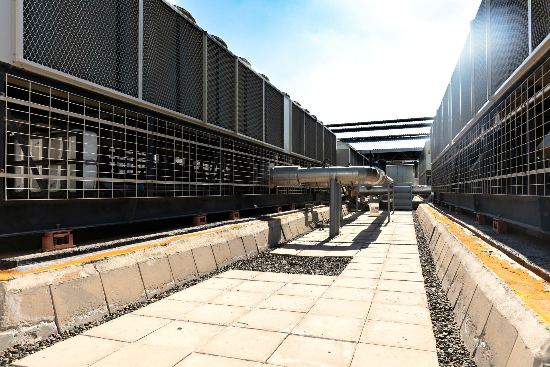 View of a large industrial cooling system with metal pipes and grids outdoors under bright daylight.